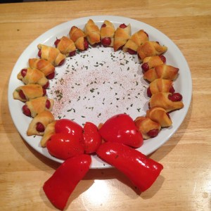 1 8oz pack of crescent rolls 1 13 oz pack of Hillshire, beef smokies 1 red pepper *1 tsp garlic salt *parmesan cheese *salt and pepper *parsley Preheat oven to 375 degrees.  The pack of crescent rolls comes in 8 triangles; we are going to cut each triangle into 4 small triangles, making 32 small triangles.  **I sprinkle the dough with garlic salt, parmesan cheese, salt and pepper before I add the smokies.**  Take one smokie, place at the bottom of a triangle, and roll up until you can press the dough together creating the "pig in a blanket".  Continue this process until all triangles have been used.  Bake on a non-stick cookie sheet for 10-15 minutes (it took mine about 16 minutes to brown).   Red Pepper Bow: Hollow out a red pepper removing all seeds.  Cut the pepper into a shape of a bow.  I used the top of the bell pepper to create the "bow" part and middle "flat" part of the pepper to create the "ribbon".  I also roasted the red pepper because it can be cut and eaten with the pigs in a blanket.  To do this, preheat oven to 400 degrees.  Coat the red pepper in olive oil, salt, and pepper.  Bake for approximately 15-20 minutes, depending on how soft you want the pepper.  To assemble the bow, I used toothpicks. :)  It is a lot easier than it looks. Assembly: Line a round plate with the pigs in a blanket and top with the roasted red pepper bow.